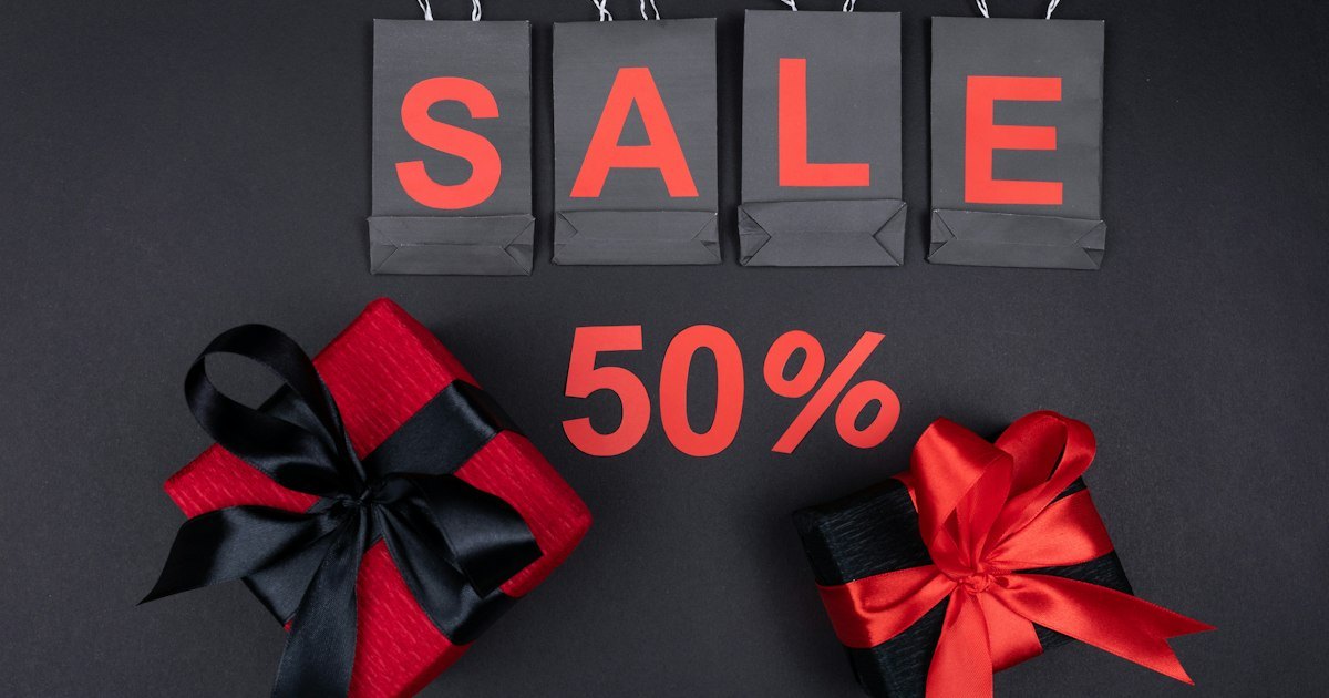 Flat lay of black shopping bags reading SALE with a 50 percent sign and two red gift boxes tied with ribbon