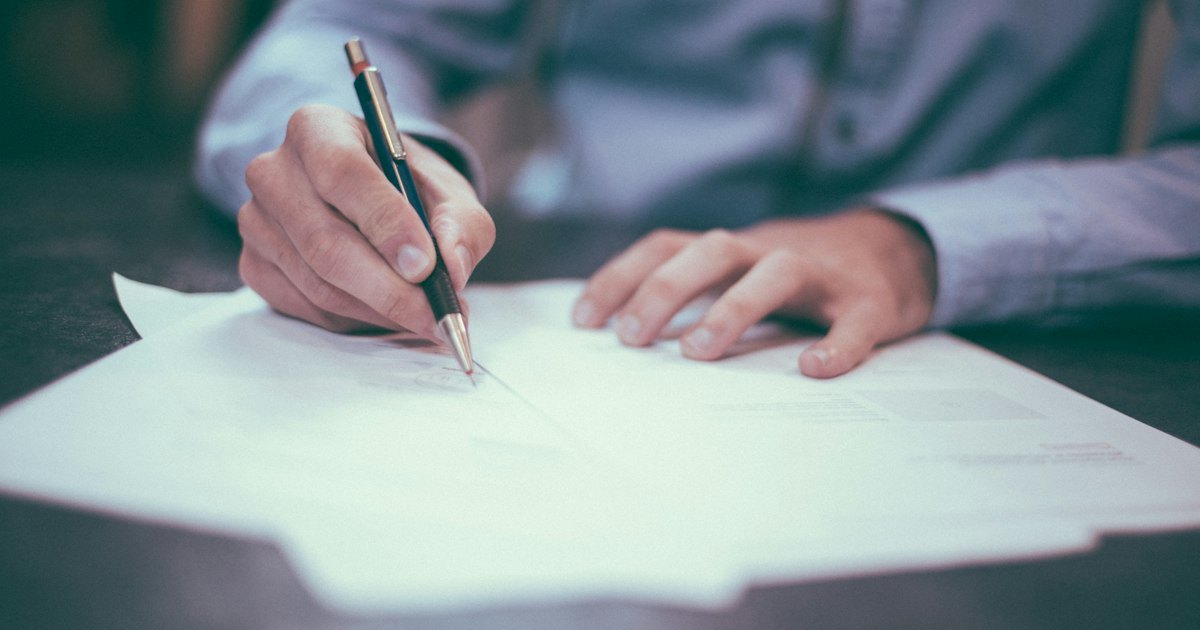Close-up of a person signing a printed document with a pen on a desk