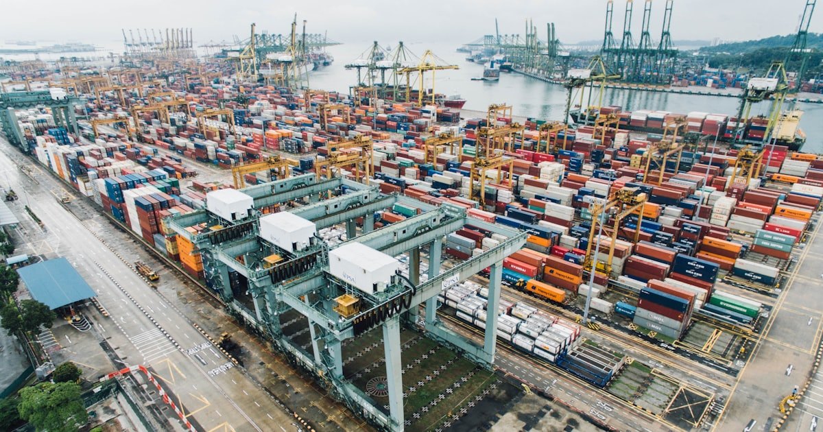 Stacked shipping containers and port cranes at a container terminal, seen from above