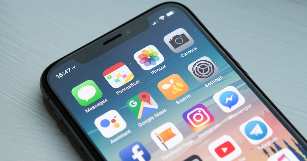 A smartphone held up against a blurred outdoor background, showing its home screen filled with app icons